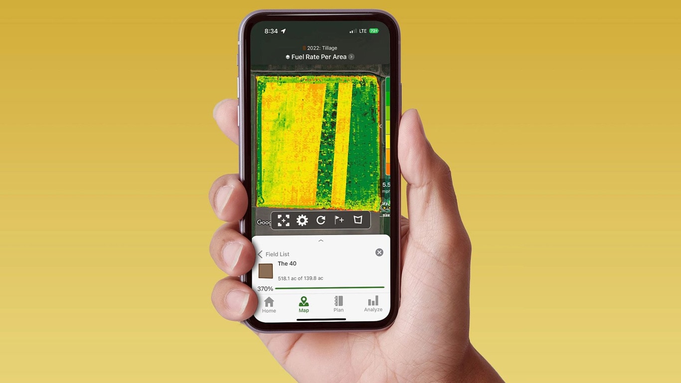 Dłoń trzymająca smartfon wyświetlający John Deere Operations Center z danymi na temat zużycia paliwa.