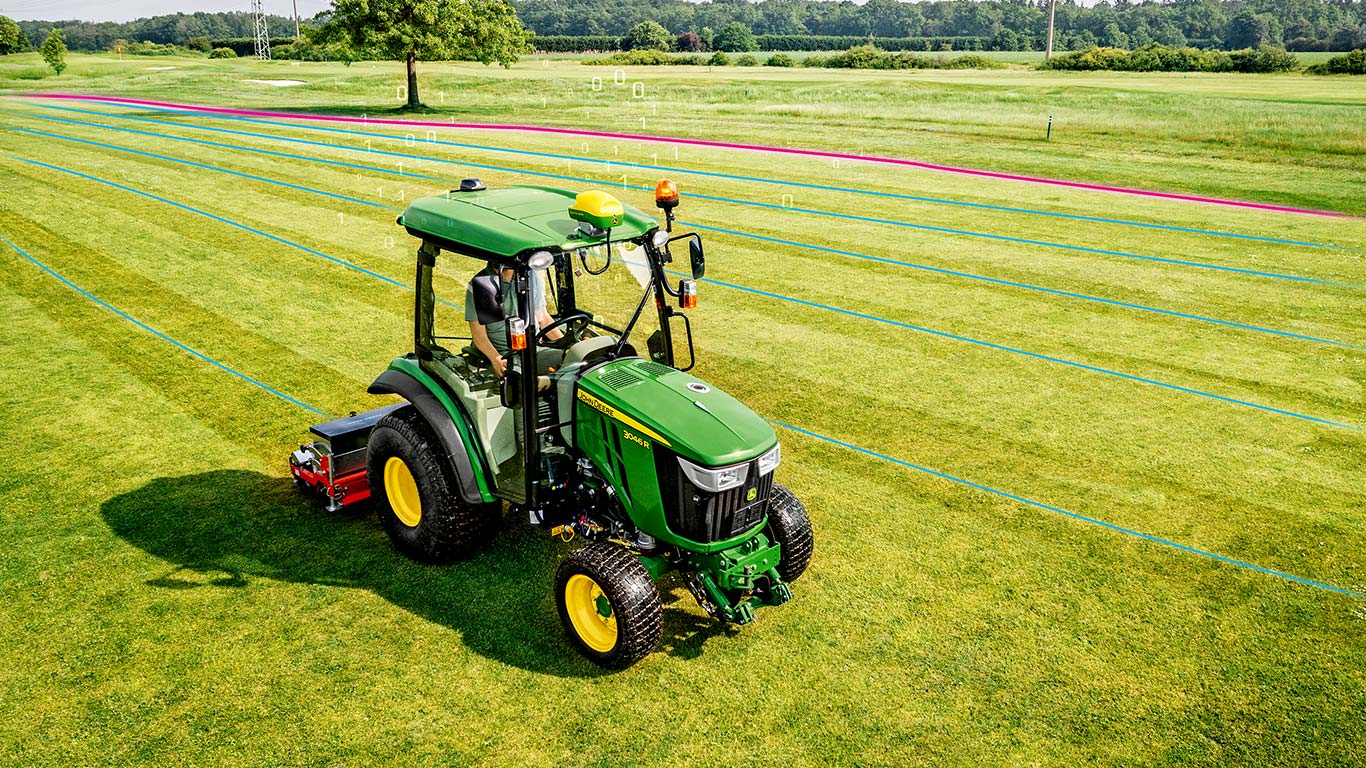 Greenkeeper na obszarze murawy z kompaktowym ciągnikiem użytkowym John Deere.
