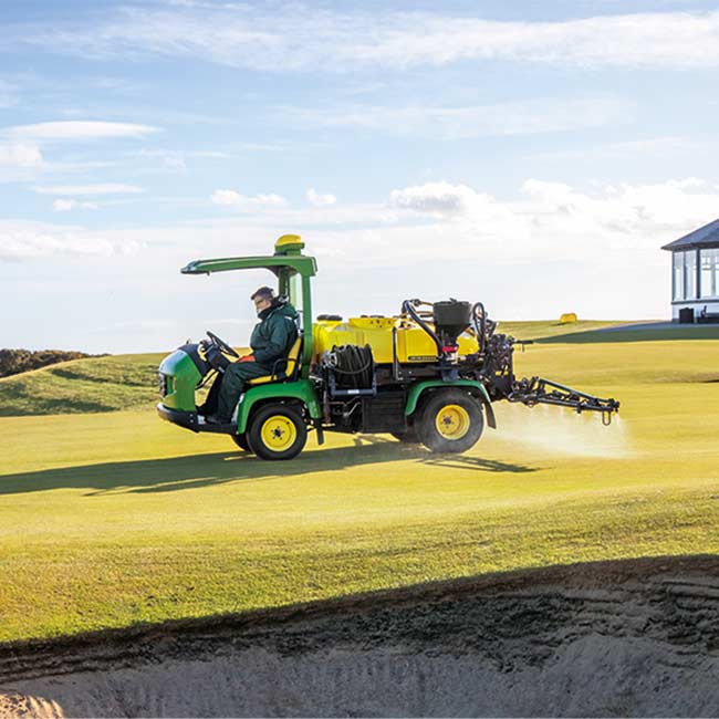Konserwator pól golfowych pracuje na terenie zielonym z opryskiwaczem John Deere