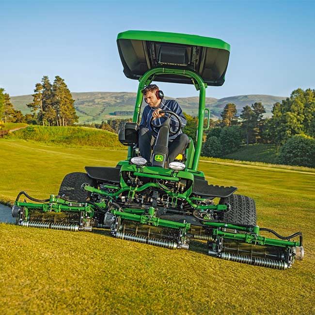 Konserwator pól golfowych pracuje na obszarze murawy z kosiarką do green John Deere, widok od przodu.