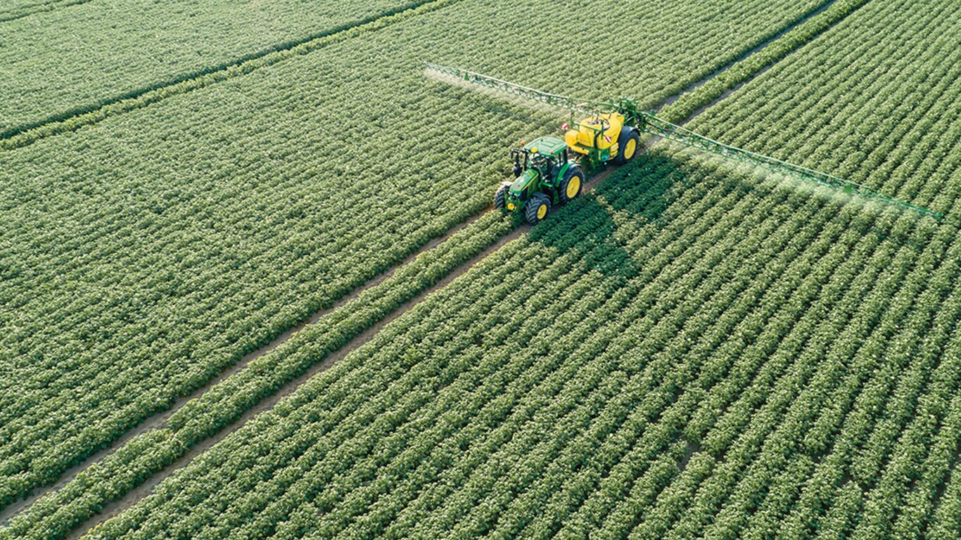 Ciągnik John Deere serii&nbsp;6M ciągnący opryskiwacz doczepiany M700 na polu ziemniak&oacute;w