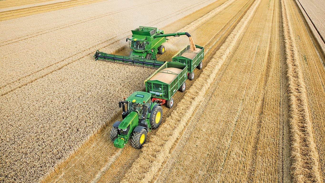 Kombajn John Deere serii&nbsp;S wyładowujący pszenicę do podw&oacute;jnych przyczep ciągniętych przez ciągnik