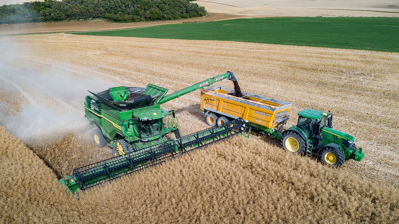 Kombajn John Deere serii&nbsp;X wyładowujący rzepak do przyczepy do ziarna ciągniętej przez ciągnik John Deere